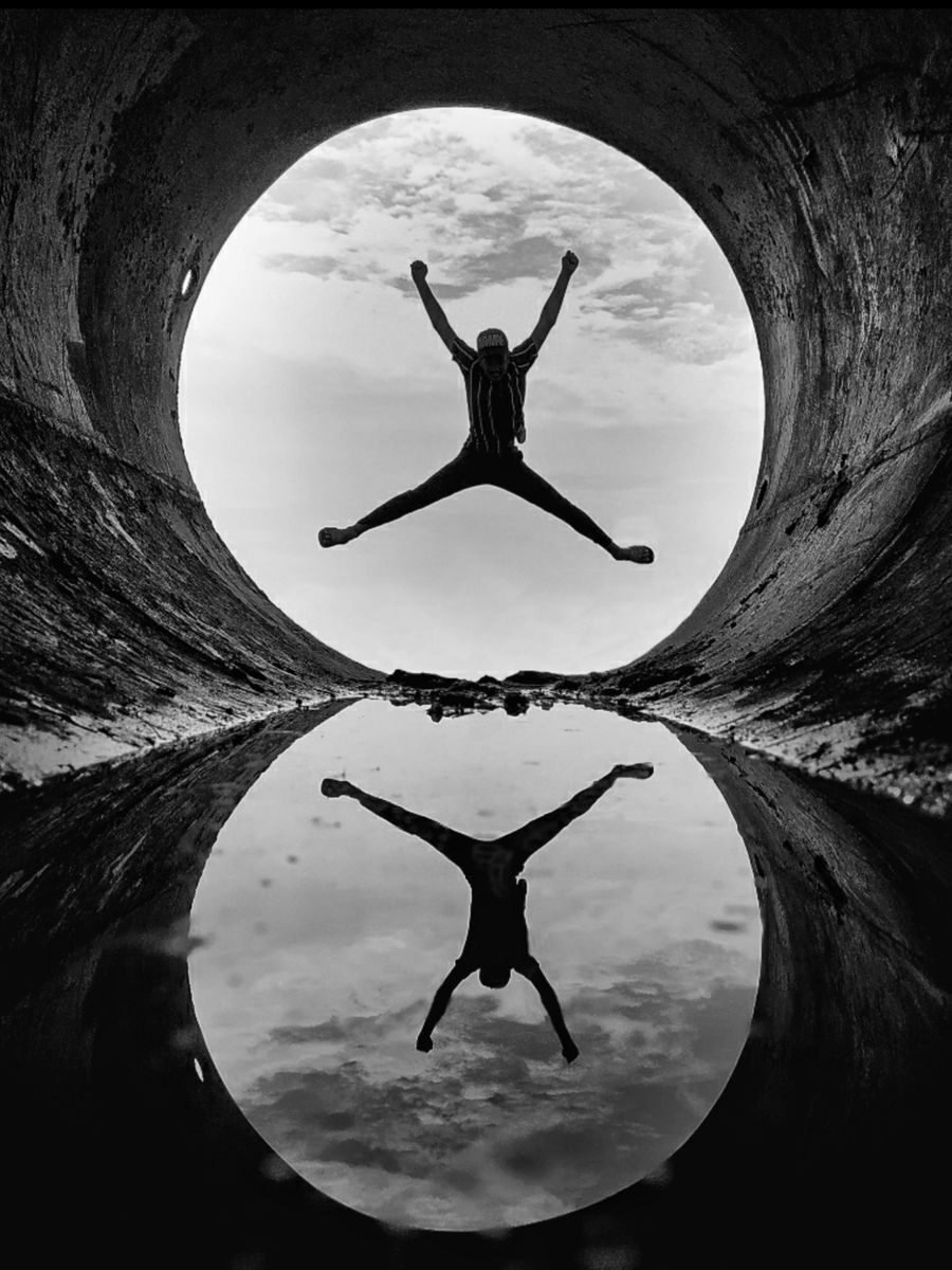 Black and white silhouette of a person jumping with a reflection in a tunnel.